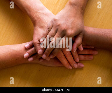 looking down on four fifty year old female hands placed ontop of each other, the top hand and third hand are Asian and the second and fourth hand are  Stock Photo