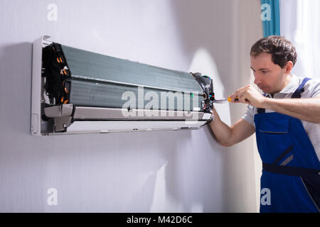 Male Technician Repairing Air Conditioner With Screwdriver Stock Photo