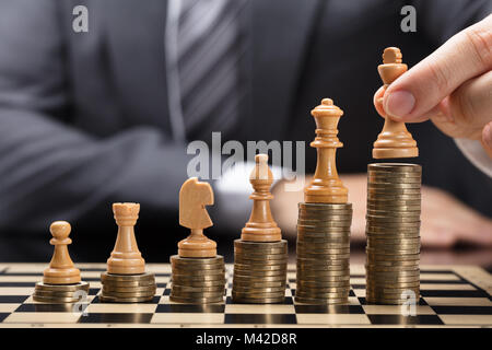 Close-up Of Businessperson's Hand Placing Brown Chess Pieces On Stacked Coins Stock Photo