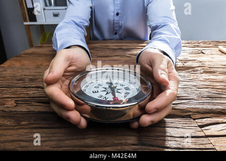Close-up Of A Businessperson's Hand Holding Compass On Wooden Desk Stock Photo