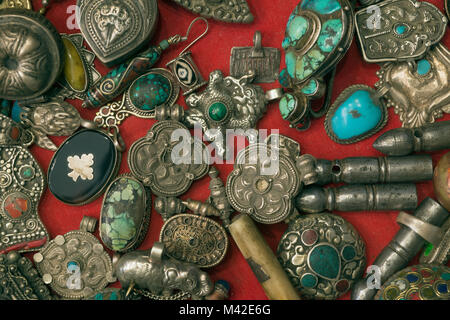 Tibetan religious silver and copper jewelry: earrings, amulets, turquoise stones and lapis lazuli on a red background in an antique store. Stock Photo