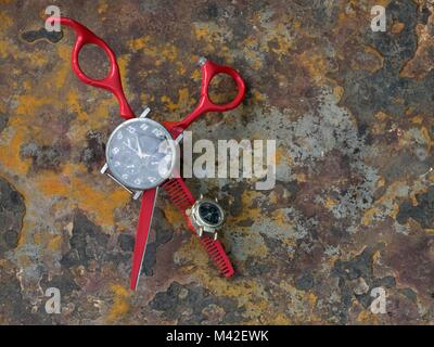 Red stylish hairdresser scissors with graceful handles on rusty background, in the middle of the instrument lie a black wristwatch with broken glass. Stock Photo