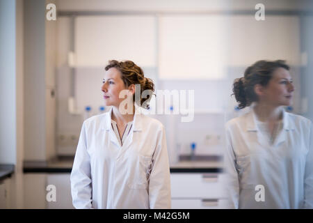 Female scientist looking out of window with reflection Stock Photo
