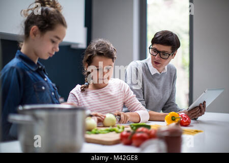 Mum teaching daughters a recipe using a digital tablet Stock Photo