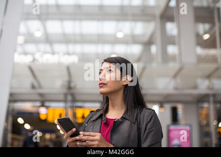 Commuter looking at train times at station holding smartphone Stock Photo