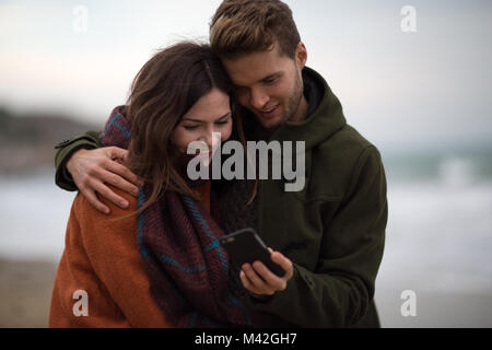 Young adult couple looking at smartphone on beach Stock Photo