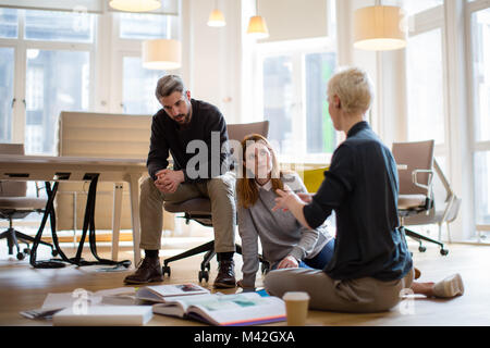 Group of designers discussing ideas with paperwork on office floor Stock Photo