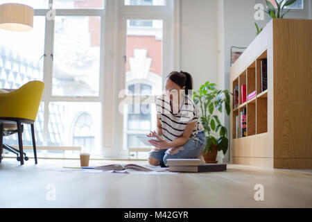 Female designer working on ideas with digital tablet and paperwork on office floor Stock Photo