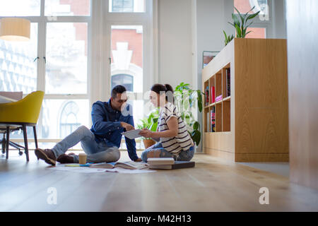 Colleagues working on ideas with digital tablet and paperwork on office floor Stock Photo