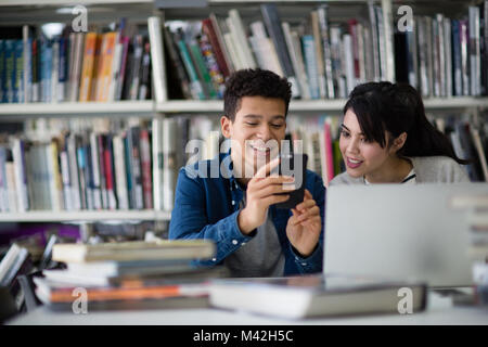 Students looking at smartphone in library Stock Photo