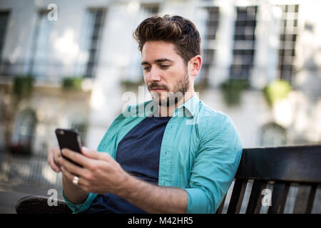 Tourist sitting on bench in London looking at smartphone Stock Photo