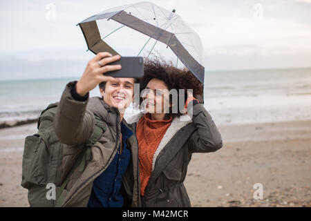 Young couple taking a selfie on a beach in bad weather Stock Photo