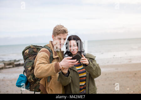 Young couple using smartphone on a winter break at beach