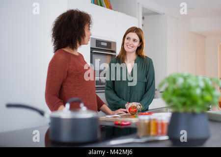 Friends socialising in a kitchen whilst cooking Stock Photo