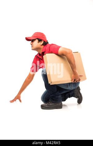 Delivery Concept - Portrait of Happy Indian or delivery man in red or green uniform walking or jumping or checking or presenting cardboard box with co Stock Photo