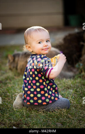 A young toddle enjoys a fruit snack of orange slices and bananas in a back yard garden. Stock Photo