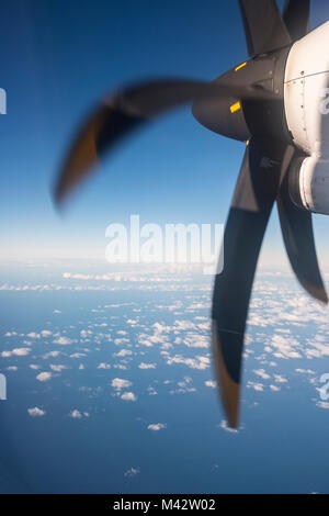 On the way - looking at aeroplane propeller from the aircraft window seat with blue sea and white clouds below Stock Photo