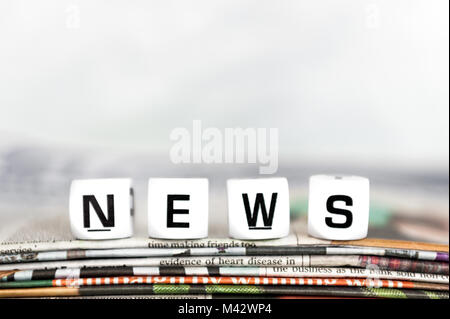 News spelt out in letter cubes on a pile of newspapers with white background and copy space. News concept. Stock Photo