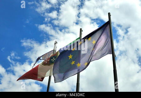 The flag of the EU flying beside the Italian naval flag against a blue and cloudy white sky Stock Photo