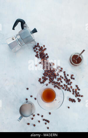Pouring coffee beans from Moka pot in a glass espresso cup with a saucer. Creative top view hot drink concept with copy space. Stock Photo