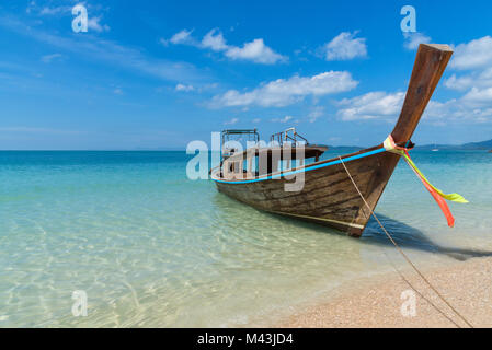 Stunning landscape shot of a paradise destination- lone longtail boat at the shore of a sandy beach in Thailand with clear blue ocean water Stock Photo