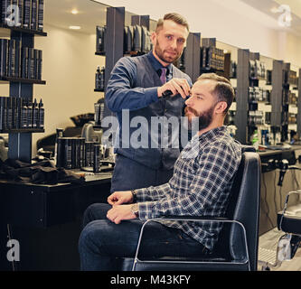 Stylish male hairdresser doing haircut to a bearded male in a sa Stock Photo