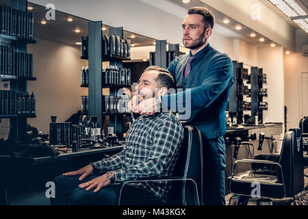 Hairdresser doing haircut to a bearded man in a barbershop. Stock Photo
