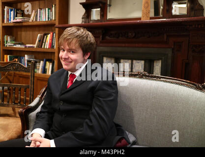 A young man smiling in a suit sat on a sofa taken from the side Stock Photo