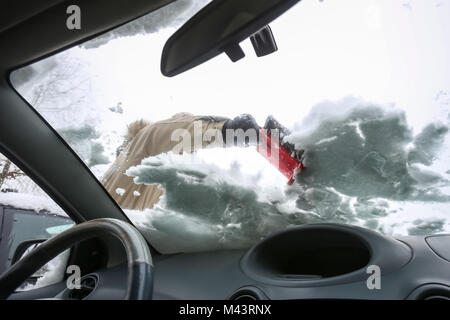 A woman cleaning the snow off the windshield viewed from the inside of the car. Stock Photo