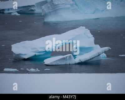 A small iceberg with an archway floating in Charlotte Bay in Antarctica. Dense clouds are overhead and steel gray water in the foreground. Stock Photo