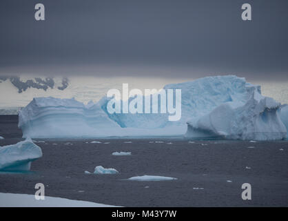 A large iceberg with fissures and ridges floating in Charlotte Bay in Antarctica. Dense clouds are overhead and choppy steel gray water in the front. Stock Photo