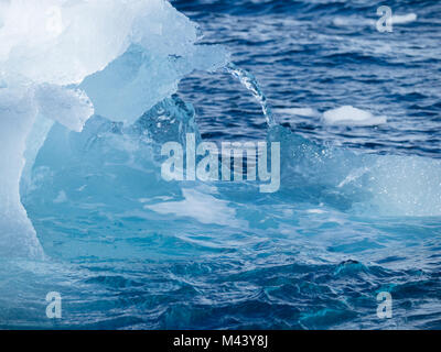 A light, medium and dark blue iceberg floating in the dark gray water of the Southern Ocean in Antarctic Sound. Overcast sky is above. Stock Photo