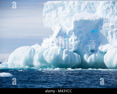 A large light blue iceberg with a foundation of spheres. The dark blue water of the Southern Ocean has small ripples. cloudy sky above. Stock Photo