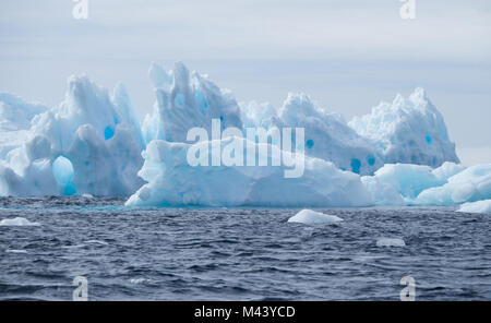 A light, medium and dark blue iceberg floating in the dark gray water of the Southern Ocean in Antarctic Sound. Overcast sky is above. Stock Photo