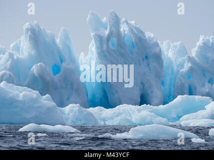 A light, medium and dark blue iceberg floating in the dark gray water of the Southern Ocean in Antarctic Sound. Overcast sky is above. Stock Photo