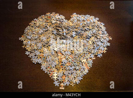 Jigsaw puzzle pieces piled on a dark wood table in the shape of a heart. Stock Photo