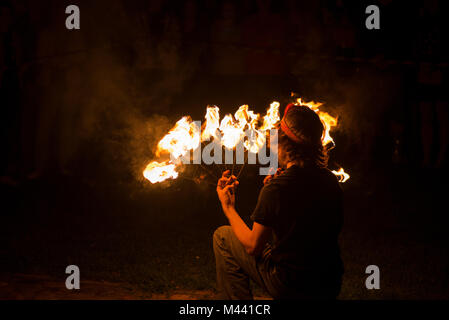 Young male performing fire juggling in front of excited crowd. Fire show and performance at night. Stock Photo