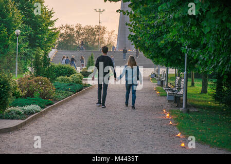 Happy couple holding hands and walking in park on lit candle path during sunset. Romantic summer evening, love is in the air. Stock Photo