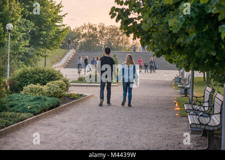 Happy couple holding hands and walking in park on lit candle path during sunset. Romantic summer evening, love is in the air. Stock Photo