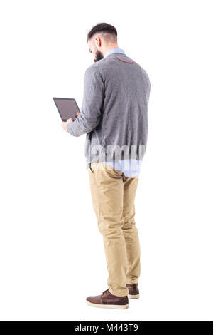 Rear view of stylish bearded businessman using tablet pad computer. Full body length portrait isolated on white studio background. Stock Photo
