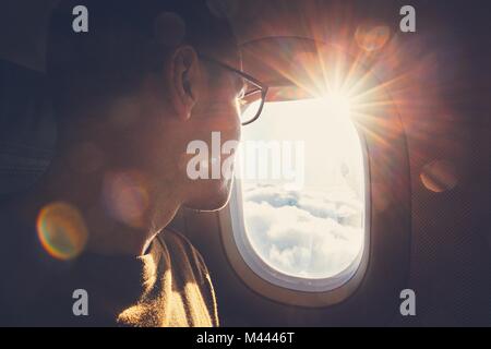 Young man looking out through window of the airplane during beautiful sunrise. Stock Photo