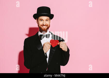 Smiling man in a tuxedo and top hat holding a red heart Stock Photo