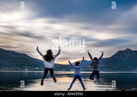 Rear view of boy and young women jumping mid air by river at dusk, Vercurago, Lombardy, Italy Stock Photo
