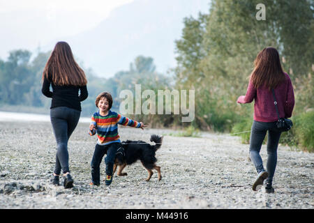 Boy with young women running with dog along riverside, Calolziocorte, Lombardy, Italy Stock Photo