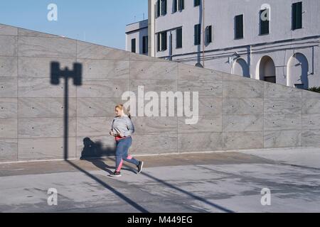 Curvaceous young female runner running along sidewalk