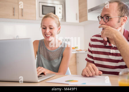 Young woman and boyfriend doing paperwork and using laptop at table Stock Photo