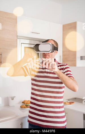 Mature man looking through virtual reality headset in kitchen Stock Photo