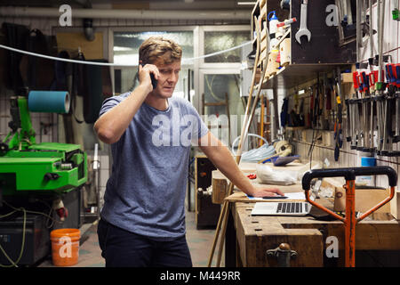 Man in workshop, using smartphone, looking at laptop Stock Photo