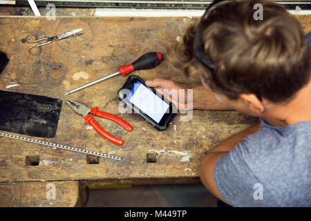 Man in workshop, using smartphone, overhead view Stock Photo
