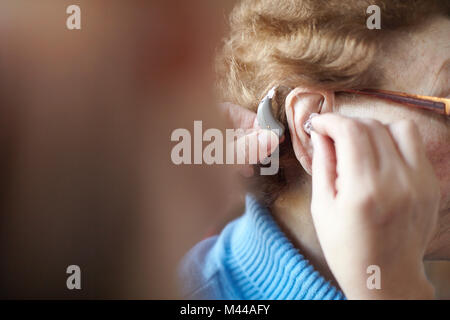 Mature woman helping senior woman insert hearing aid, close-up, differential focus Stock Photo